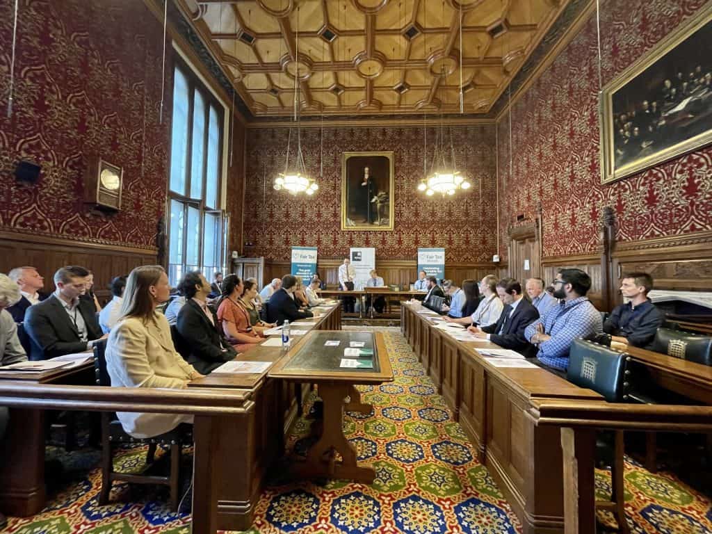 committee room in Parliament with people sitting facing each other and a panel